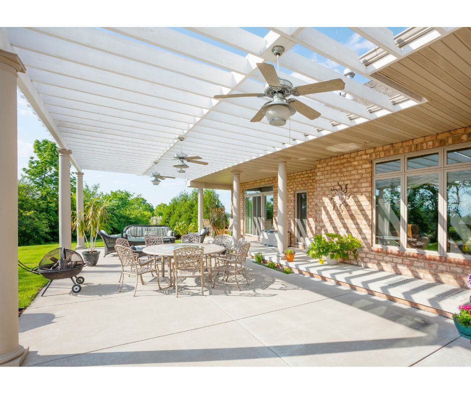 Outdoor concrete patio with pergola, table, chairs, and barbecue grill on a sunny day.