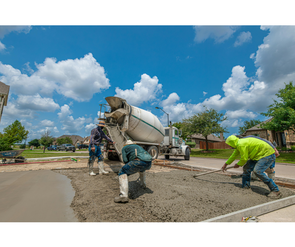 Concrete workers using a truck-mounted mixer on a driveway with a blue sky and clouds in the background.